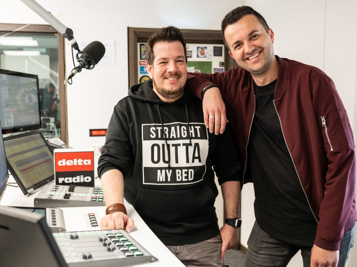 delta radio Frau und Mann sitzen lächelnd auf der Couch vor einer Logowand von delta radio.